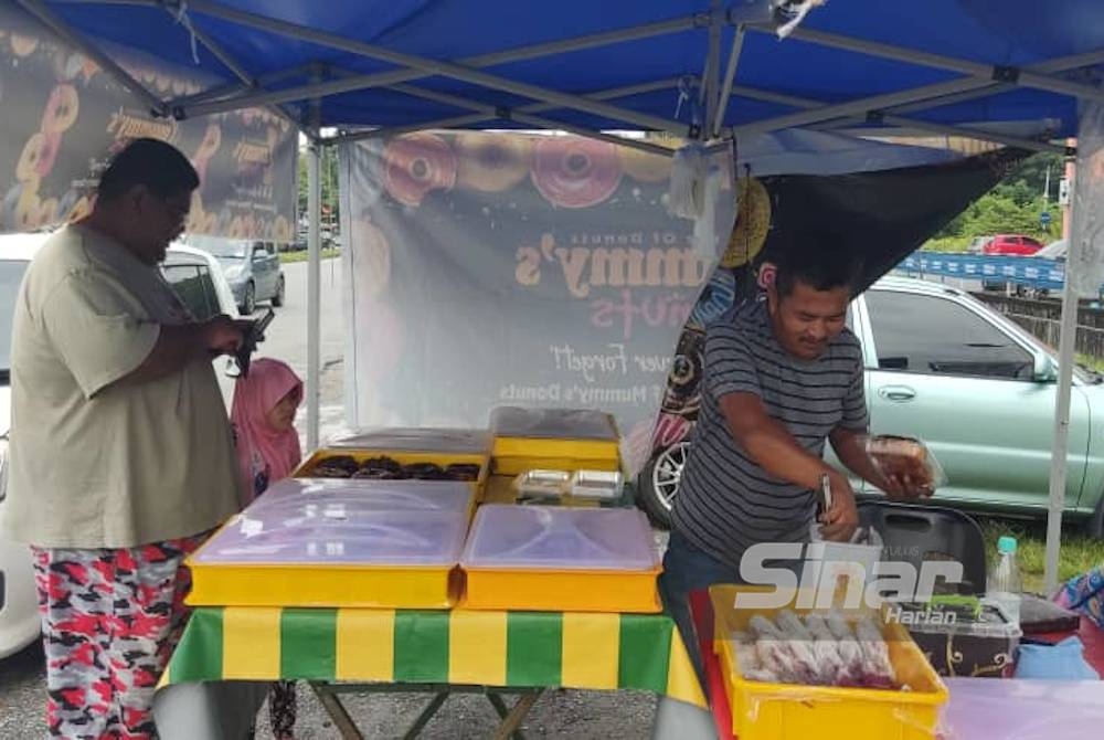 Mohd Zaini (kanan) membungkus donat untuk pelanggan di gerainya di Alor Setar pada Sabtu.