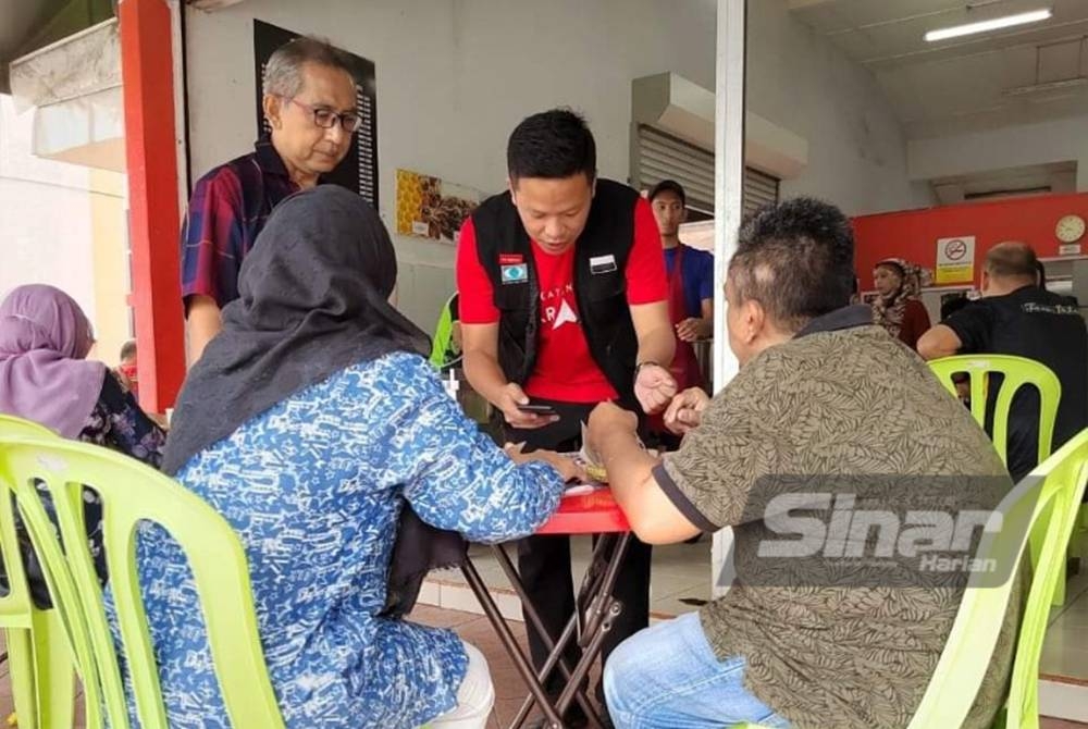 Zuraidi (berdiri, kiri) menyantuni pengundi di Parlimen Indera Mahkota pada Isnin.
