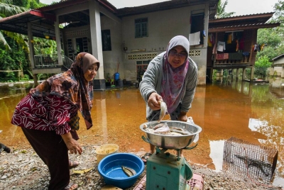 Penduduk kampung, Laila Mohd Nor, 38, (kanan) sedang menimbang ikan untuk dijual kepada Salmah Che Husin, 63, (kiri) selepas memasang jaring pukat di kawasan kediamannya yang digenangi air ketika tinjauan di Kampung Tersang, Rantau Panjang pada Ahad. - Foto Bernama