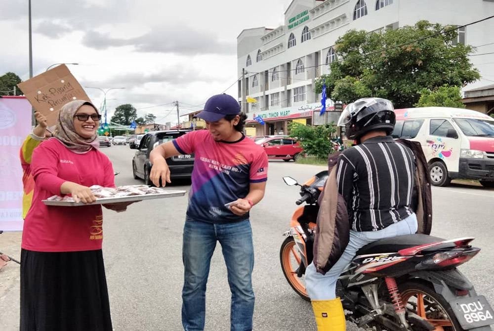 Aiman (kanan) mengagihkan kek pisang kepada penunggang motosikal di Jalan Pintu Geng pada Rabu.