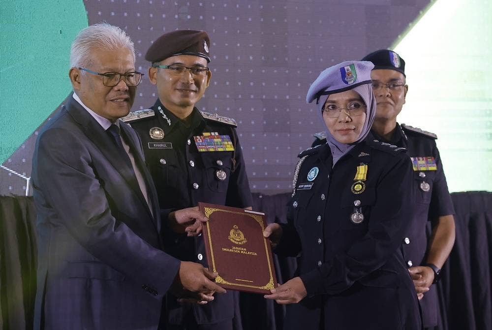 Hamzah (kiri) menyampaikan anugerah perkhidmatan khas kepada Penguasa Imigresen Johor, Noor Haironi Ngadirin pada Majlis Perhimpunan Jabatan Imigresen di Putrajaya pada Jumaat. - Foto Bernama