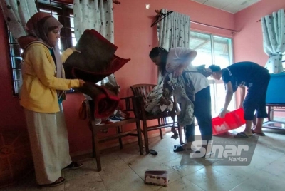 Norlaila (kiri) mengemas rumahnya yang dilanda banjir kilat.