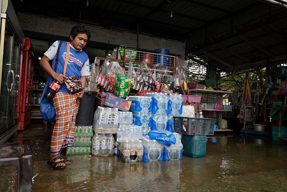 Seorang penduduk membeli barang keperluan dari sebuah kedai runcit yang dilanda banjir ketika tinjauan di sekitar Klang, hari ini.