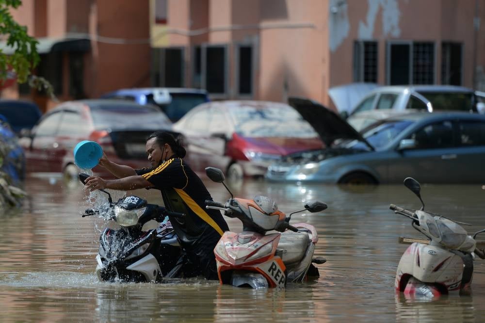 Seorang lelaki membersihkan motosikalnya yang diselaputi lumpur selepas dua hari ditenggelami air di Shah Alam.