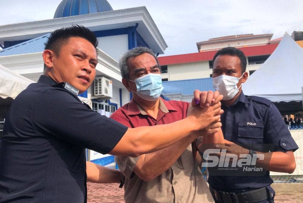 Che Mustapa (tengah) dibantu dua anggota menunjukkan jari telunjuk yang berdakwat selepas selepas mengundi awal.