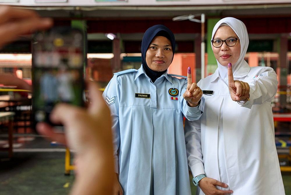 Anggota Tentera Udara Diraja Malaysia (TUDM) Koperal Nur Syazwani Md Yusof, 30, (kiri) yang mengandung tiga bulan dan anggota Tentera Laut Diraja Malaysia (TLDM) Laskar Kanan Siti Najah Mat Rodin, 35, (kanan) menunjukkan jari yang telah dicelup dakwat biru selepas selesai mengundi awal sempena Pilihan Raya Umum ke-15 (PRU15) di Sekolah Kebangsaan Desa Tun Hussein Onn hari ini.