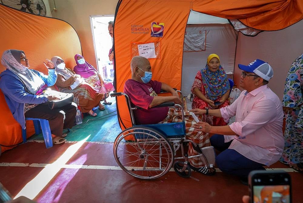 Anuar (kanan) beramah mesra dengan mangsa banjir, Abdul Samat Osman, 75 (berkerusi roda) semasa melakukan lawatan ke PPS di Dewan Komuniti Dengkil pada Khamis. - Foto Bernama