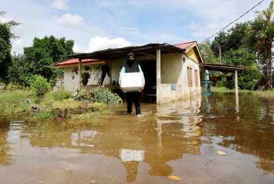 Mangsa banjir, Umi Sarah Hassan, 40, mengangkat barang untuk diselamatkan akibat bencana banjir ketika tinjauan di Kampung Asahan pada Khamis. - Foto Bernama