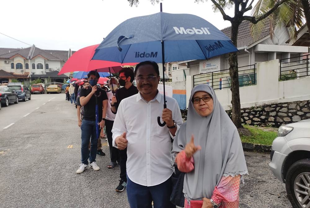 Azli (kiri) bergambar bersama isterinya ketika beratur menunggu giliran untuk masuk ke pusat mengundi di Dewan Melur, Seksyen 7, di sini, pada Sabtu.