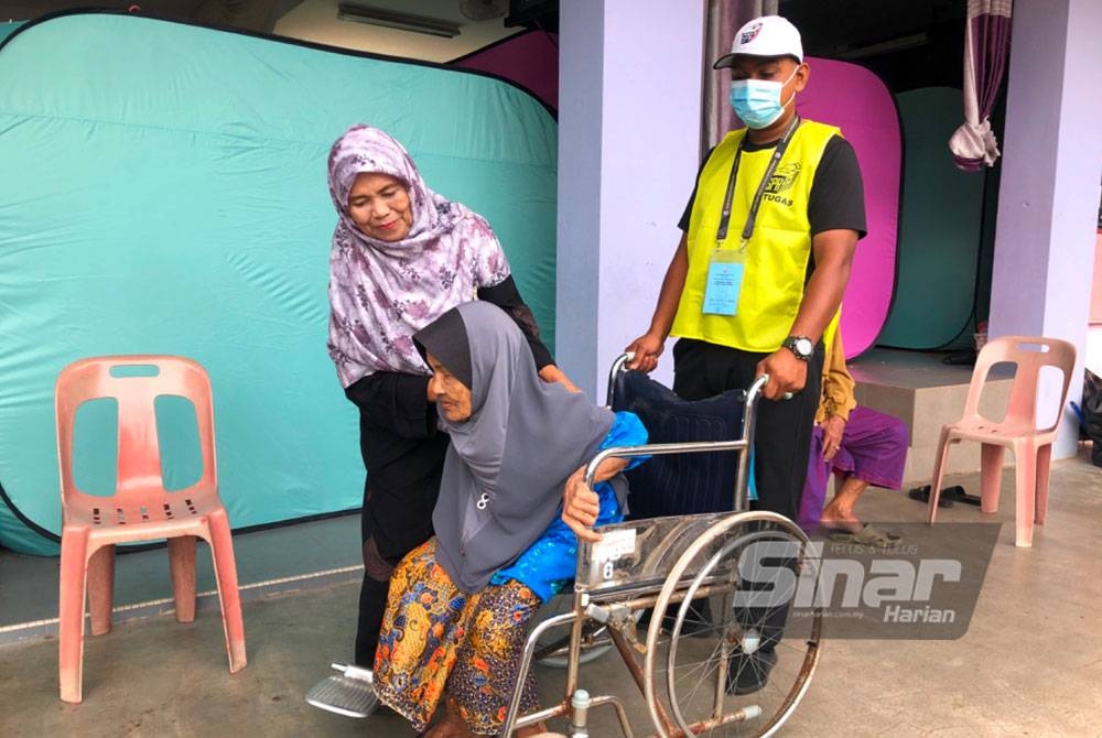Che Limah (tengah) dibantu petugas untuk pergi mengundi dengan menggunakan kerusi roda.