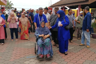 Ahmad membantu menyorong kerusi roda ibu mertuanya, Selamah, yang kurang sihat ke pusat membuang undi.