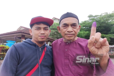 A Rani (kanan) menunjukkan jari yang dicelup dakwat khas selepas selesai mengundi di SK Bukit Diman pada Sabtu.