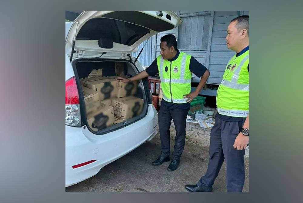 Dua penguat kuasa KPDNHEP menunjukkan minyak masak peket dalam kotak yang dipercayai cuba diseludup ke negara jiran. - Foto KPDNHEP