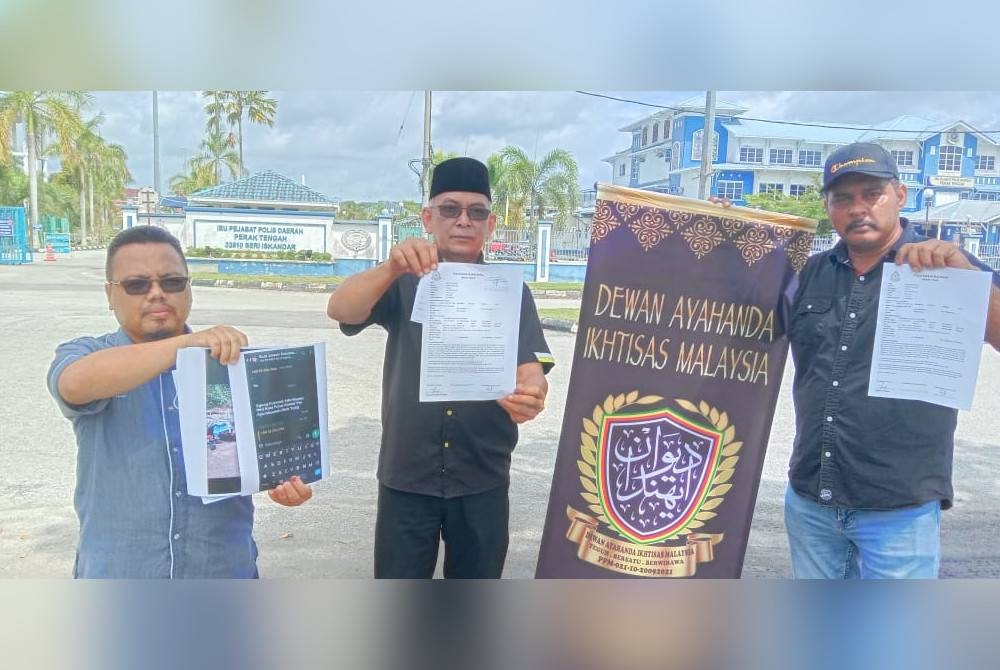 Mohamed Zainudi (au centre) montre une copie du rapport de police à Seri Iskandar mercredi.