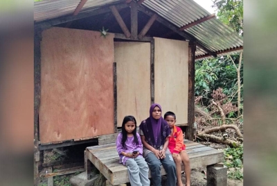 Zuraini (tengah) bersama dua anak di hadapan rumah mereka di Kampung Kuala Ayer Merah.