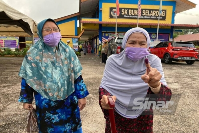 Rahmah (kanan) ditemani cucunya, Noraishah menunjukkan jari yang telah dicelup dakwat selepas selesai mengundi di SK Bukit Selarong pada Rabu.