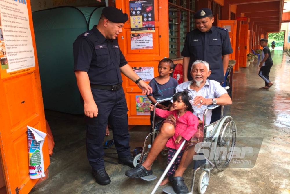 Nik Aminuddin (kiri) melawat mangsa banjir, Ibrahim Zaman yang berkerusi roda di PPS Kampung Serongga, Pasir Mas.