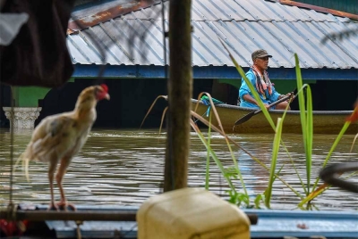 Penduduk menggunakan sampan untuk meninjau keadaan rumah mereka yang ditenggelami banjir ketika tinjauan di Kampung Tersang, Rantau Panjang pada Selasa. - Foto Bernama