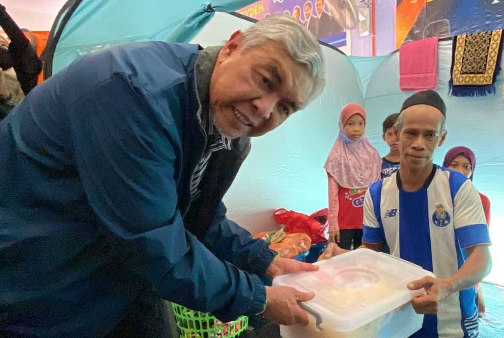 Ahmad Zahid (kiri) menyampaikan bakul makanan kepada penghuni di PPS SK Gual To'Deh di Rantau Panjang pada Khamis.