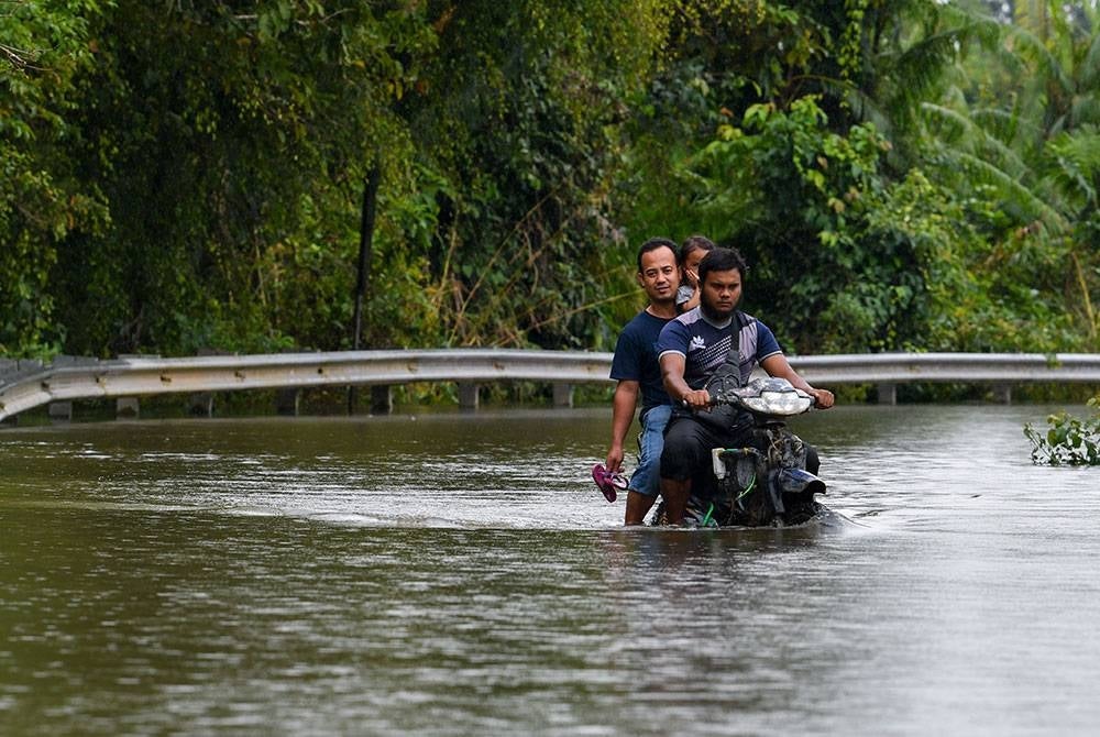 Sabri (depan) bersama rakannya Mohd Hirwan Rajiuon, 41, menunggang motosikal telah diubahsuai yang mampu meredah banjir ketika ditemui Bernama di Kampung Tersang, Rantau Panjang, pada Khamis. - Foto Bernama