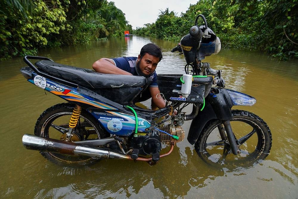 Sabri memeriksa motosikalnya yang telah diubahsuai bagi membolehkan motosikal meredah banjir ketika ditemui Bernama di Kampung Tersang, Rantau Panjang, pada Khamis. - Foto Bernama