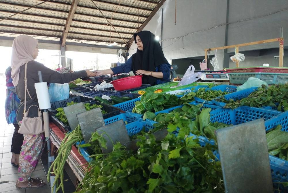 Salah seorang peniaga sayur sedang melayan pembeli yang sedang mendapatkan beberapa jenis sayuran.
