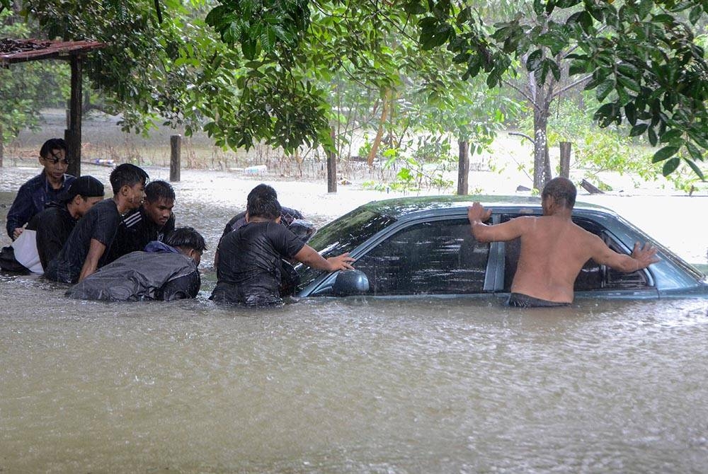 Penduduk Kampung Chawas, Shukri Ismail, 55, (kanan) dibantu penduduk setempat menolak keluar keretanya untuk dipindahkan ke tempat yang tinggi berikutan kampung terbabit dinaiki air banjir awal pagi Ahad. - Foto Bernama