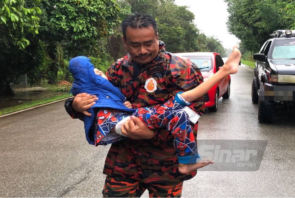 Anggota bomba memangku seorang kanak-kanak OKU yang terjejas banjir untuk dipindahkan ke PPS.
