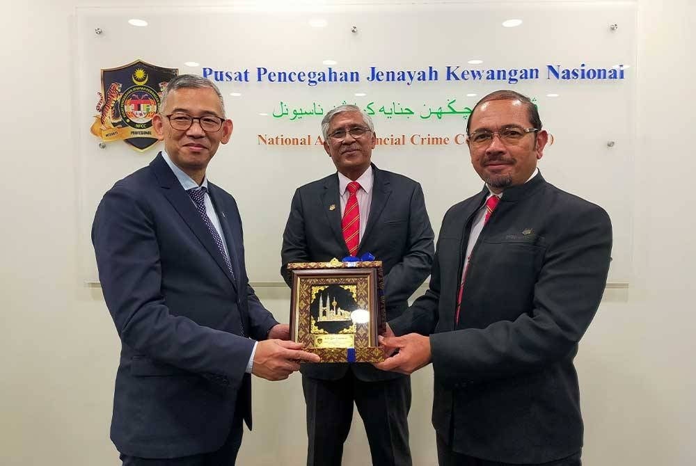 Mustafar (kanan) menyerahkan cenderamata kepada Danny Woo, disaksikan oleh Abu Kassim di Putrajaya pada Selasa.