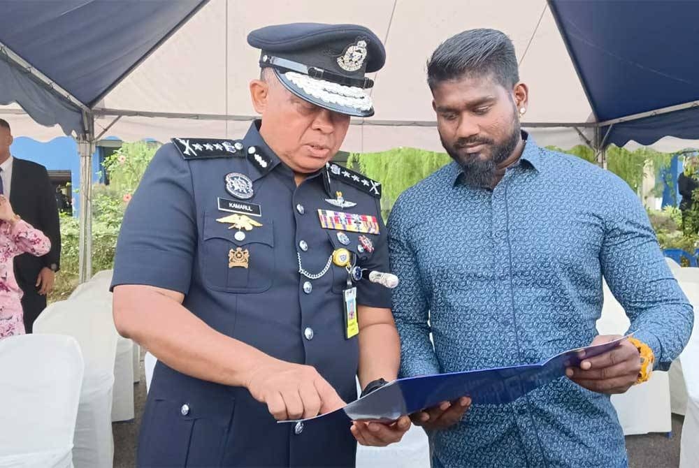 Kamarul Zaman (kiri) melihat sijil penghargaan yang diterima Muruga selepas Majlis Perhimpunan Bulan Disember 2022 di Dataran Kawad, IPK Johor, Johor Bahru pada Selasa.