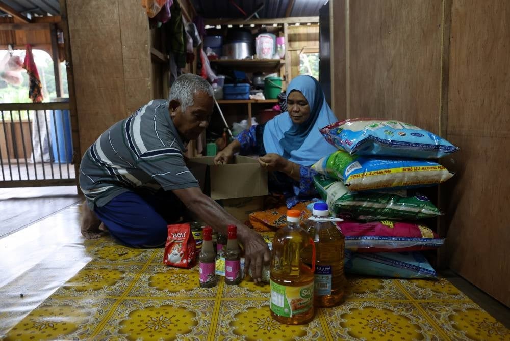 Pokwe bersama isterinya Patimah Salleh, 61, menyusun stok barang makanan asas untuk bekalan keluarganya bagi tempoh beberapa hari disebabkan mereka sekeluarga tidak berpindah ke PPS kerana tinggal di rumah terapung yang dibinanya sendiri di Kampung Terbak Batu 16 Chukai. - Foto Bernama