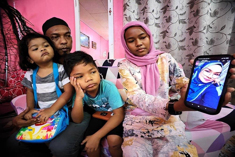 Nur Qaleesya (kanan) menunjukkan gambar Allahyarham Norazmira. Turut kelihatan Mohamad Nazrul (kiri) bersama dua lagi anaknya.