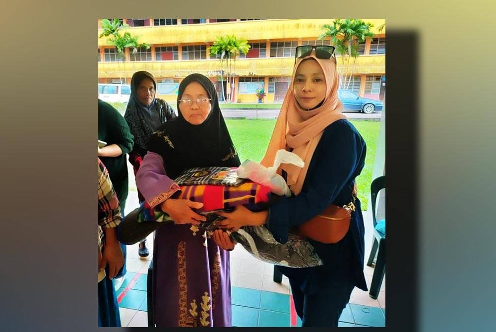 Noor Azlina (kanan) mengagihkan bantuan kepada mangsa banjir.