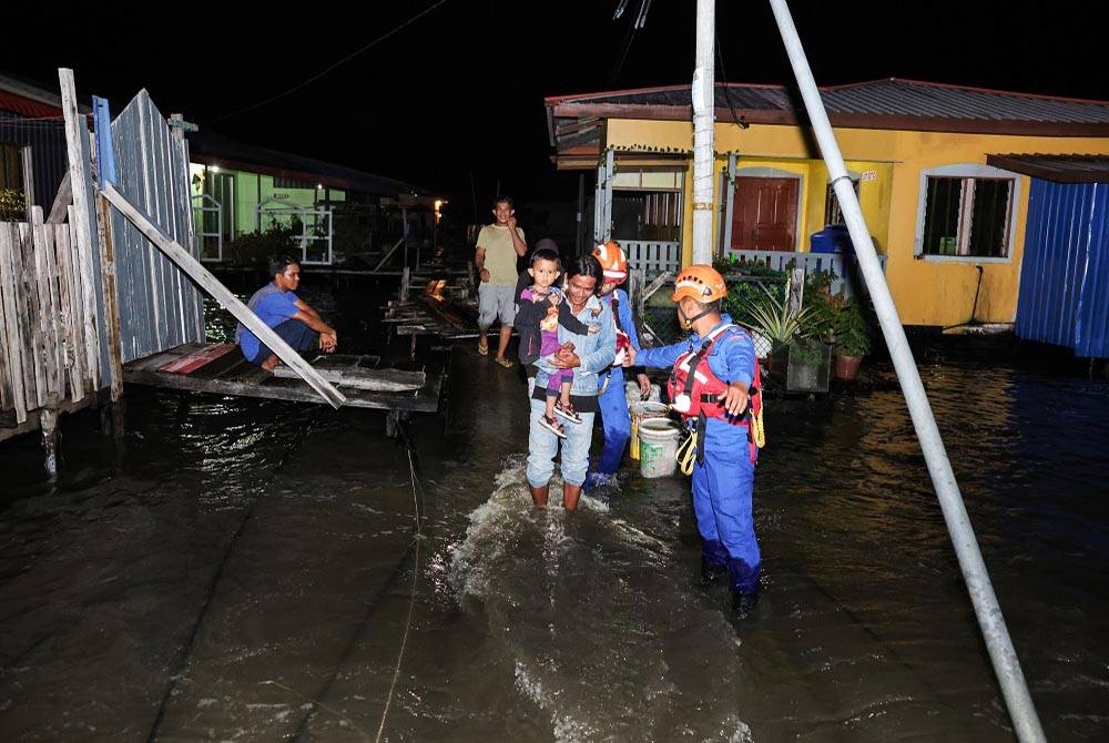 Des membres de la Défense civile (APM) ont aidé les habitants à traverser un pont qui avait été immergé dans l'eau de mer pour se déplacer vers un endroit sûr tout en surveillant le phénomène des marées hautes à Kampung Tinusa Dua la nuit dernière.  La photo de Bernama