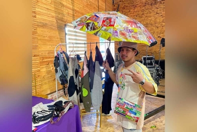 Ahmad Afiq memperagakan payung dan beg tangan yang diperbuat daripada plastik pembungkus roti, mi segera dan makanan ringan hasil kreativiti menerusi kaedah kitar tinggi atau 'upcycle'.- Foto Bernama.