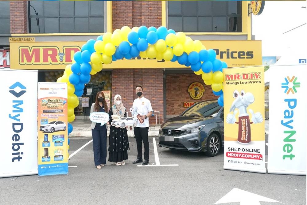 Siti Rohani (tengah) menerima replika kunci daripada Goh (kanan) selepas diumumkan sebagai pemenang peraduan ‘MR. D.I.Y. x MyDebit Je’.