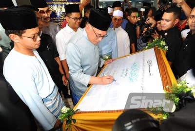 Akmal Nasrullah (tiga dari kiri) menyaksikan Anwar menandatangani plak di Masjid Jamek, Kampung Melayu Majidee, pada Jumaat.
