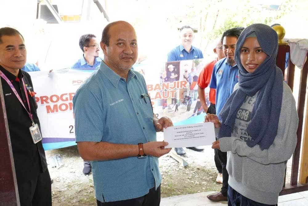 Mohd Zahari (tengah) menyampaikan sumbangan kepada seorang pelajar yang merupakan mangsa banjir di Besut.