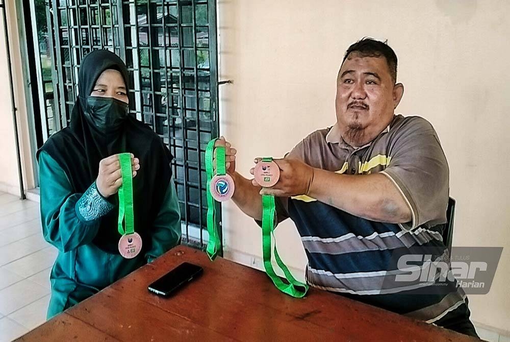 Abd Halim (kanan) dan isterinya Hartini Wagimun, 48, menunjukkan pingat yang pernah dimenangi anak mereka dalam sukan bola tampar.