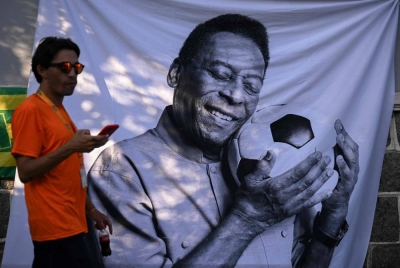 Seorang lelaki yang berkabung melewati sehelai kain dengan imej legenda bola sepak Brazil, Pele di luar stadium Urbano Caldeira, di Santos, Sao Paulo, Brazil pada Isnin. - Foto AFP
