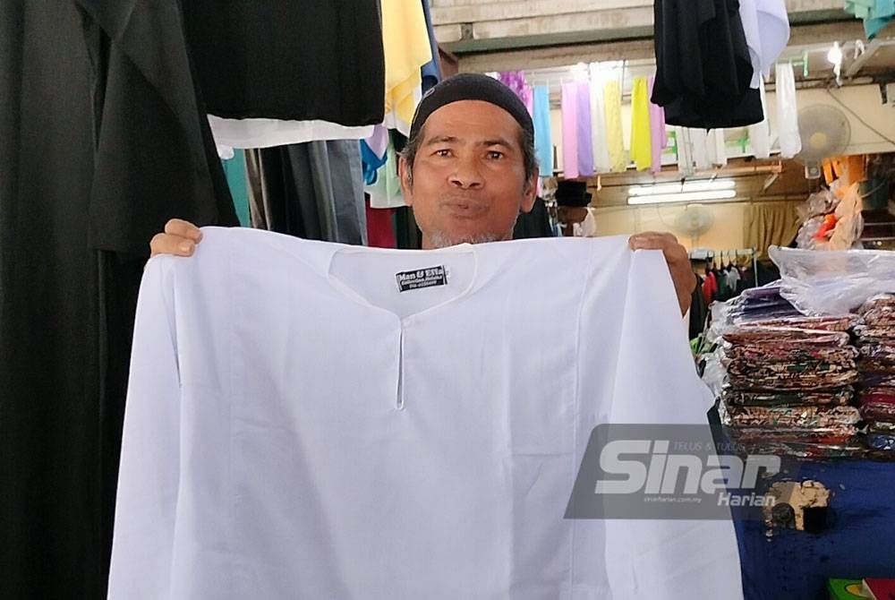 Sulaiman menunjukkan baju kurung sekolah yang dijahit dan dijual di kedainya dengan harga berpatutan.