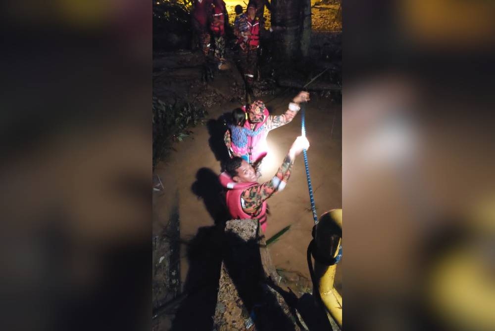 Pasukan bomba mendukung seorang kanak-kanak untuk menyeberangi sungai selepas jambatan menghubungkan rumah mereka terputus. - Foto ihsan Bomba Perak