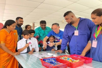 Han Pin (tiga dari kanan) membantu salah seorang murid SJKT Azad menggunakan kad debit yang diperkenalkan oleh Hong Leong Bank Bhd sambil dilihat oleh Jeevagowry (kiri).