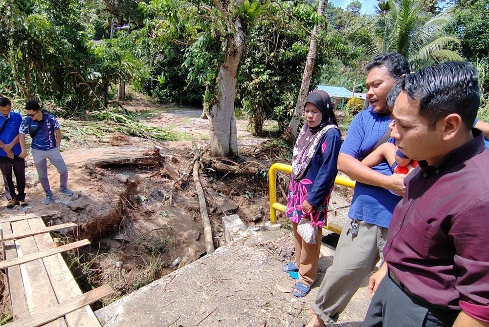 Mohd Azlan Helmi (kanan) meninjau keadaan banjir di Kampung Sahom hingga menjejaskan jambatan yang merupakan satu-satunya laluan untuk penduduk keluar.