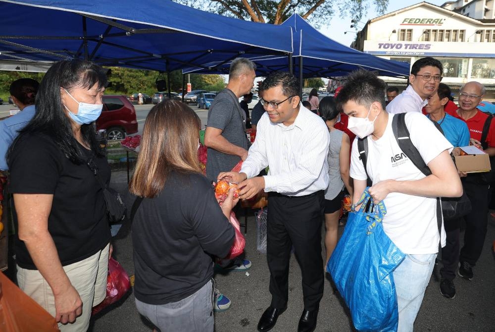 Akmal Nasrullah mengedarkan buah limau kepada orang ramai dan peniaga sempena Tahun Baharu Cina di Pasar Pagi Taman Pelangi hari ini. - Foto Bernama