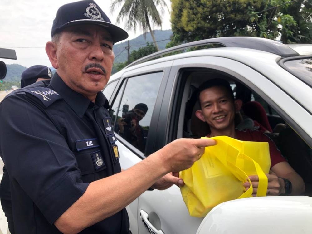 Muhamad Zaki (kiri) menyampaikan cenderamata kepada pengguna jalan raya di Bukit Yong, Pasir Puteh pada Khamis.