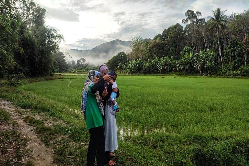 Noor Asyikin (kiri) berswafoto bersama adik dan anaknya di hadapan rumah mereka di Kampung Lubuk Tualang pada Sabtu.
