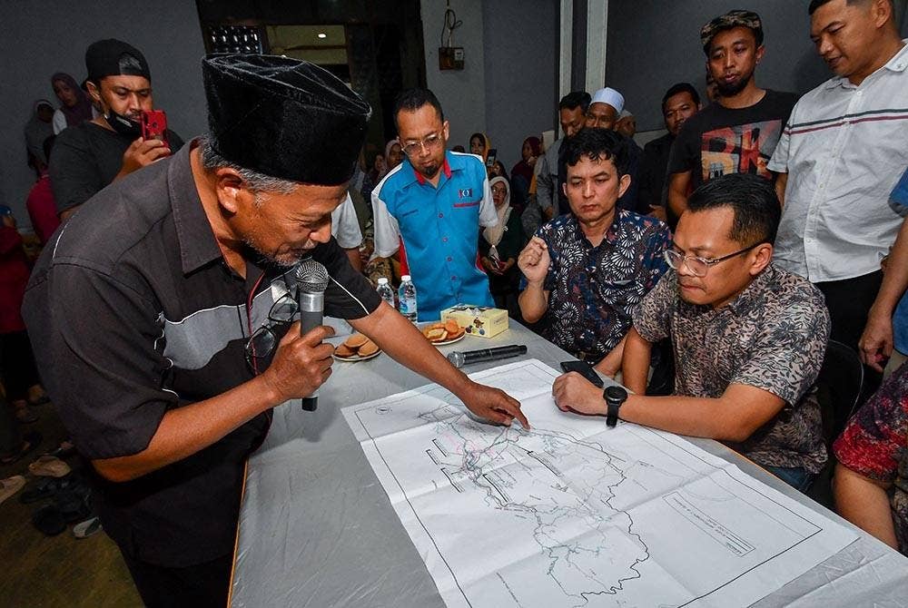 Nik Nazmi (duduk, kanan) melihat peta lokasi projek tebatan banjir yang ditunjukkan wakil penduduk, Mohd Yazid Abdullah (kiri) sewaktu hadir pada Perjumpaan Bersama Penduduk Terkesan Banjir di Kampung Tersang, Rantau Panjang pada Sabtu. - Foto Bernama