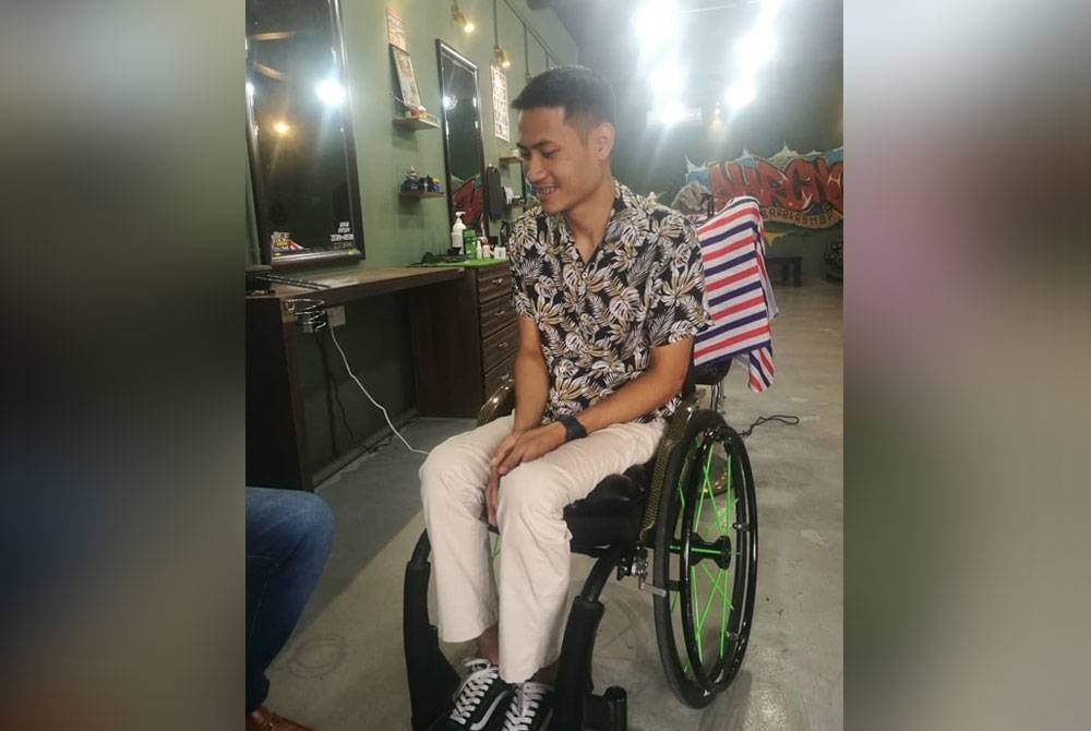 Muhammad Arif menggunakan kerusi roda jenis hidraulik bagi membolehkannya berdiri dan menggunting rambut pelanggan.