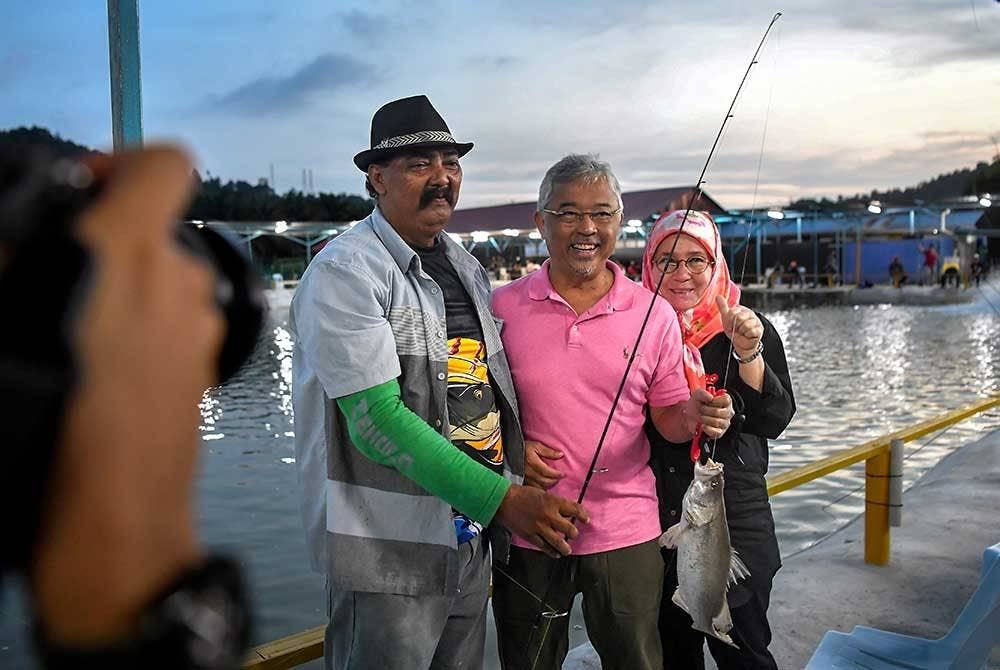 Yang di-Pertuan Agong Al-Sultan Abdullah Ri'ayatuddin Al-Mustafa Billah Shah bersama Raja Permaisuri Agong Tunku Hajah Azizah Aminah Maimunah Iskandariah berkenan bergambar bersama pemancing, Zulkifli Yussof, 58, (kiri) selepas mendapat tangkapan ikan pertama ketika aktiviti memancing di kolam pancing Afprow 1, Saujana Utama hari ini.